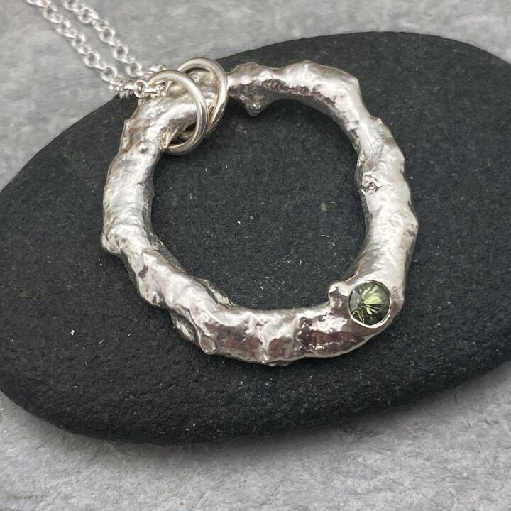 Organic silver circle pendant with a green sapphire 